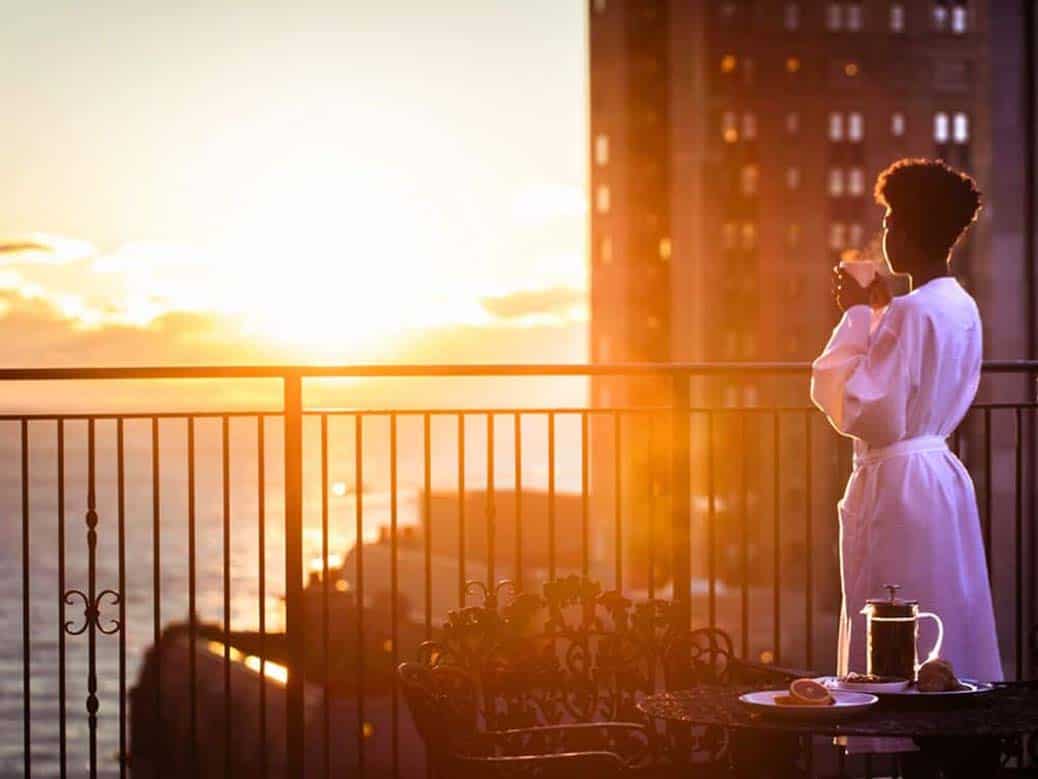 Romantic sunset hotel photo of lady in robe enjoying view from balcony of Ambassador Chicago Hotel